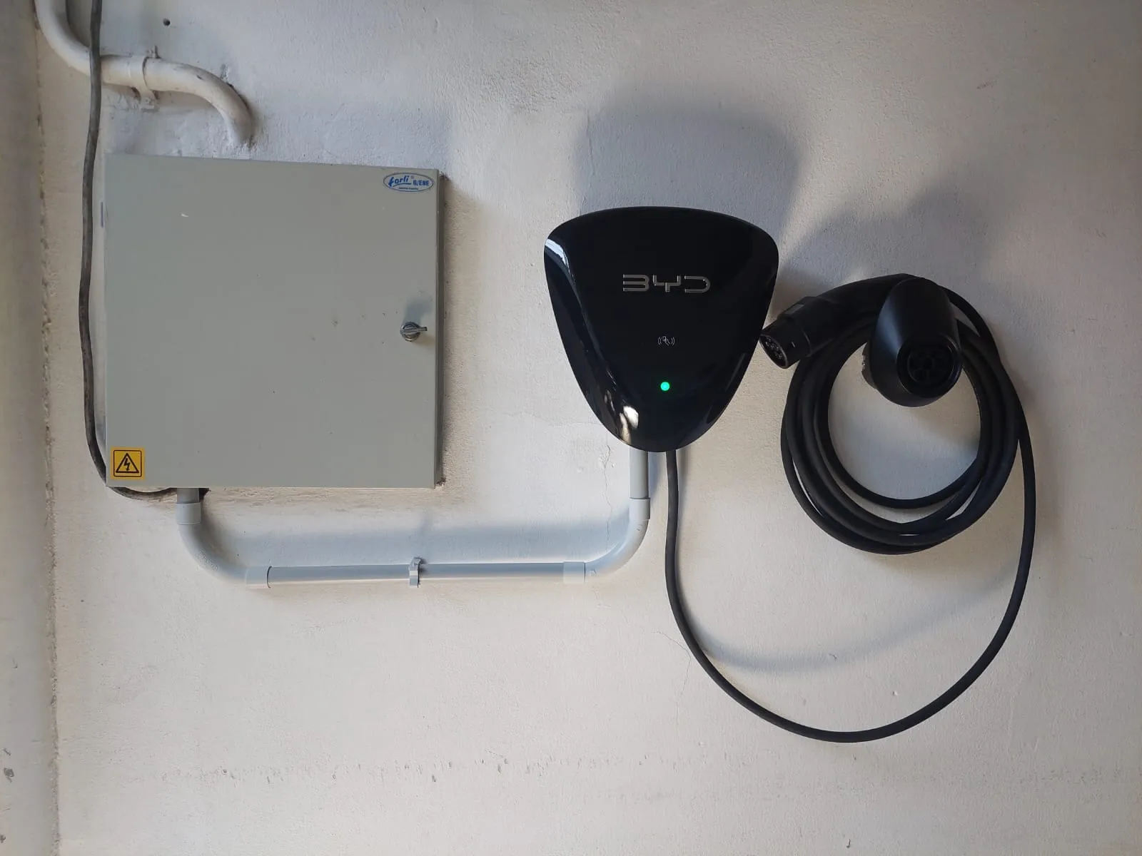 Cargador de auto eléctrico instalado en la pared junto a su tablero, con cañería prolija a la vista